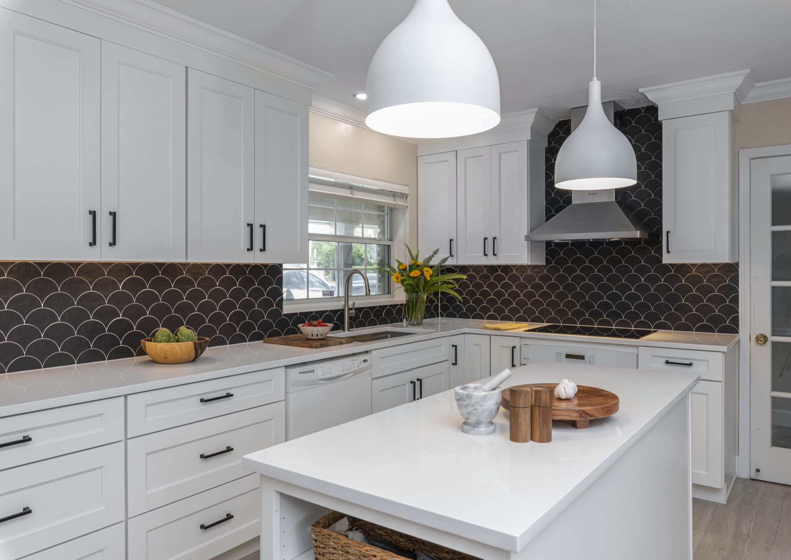 Modern kitchen interior with white cabinetry and a contrasting black tile backsplash.